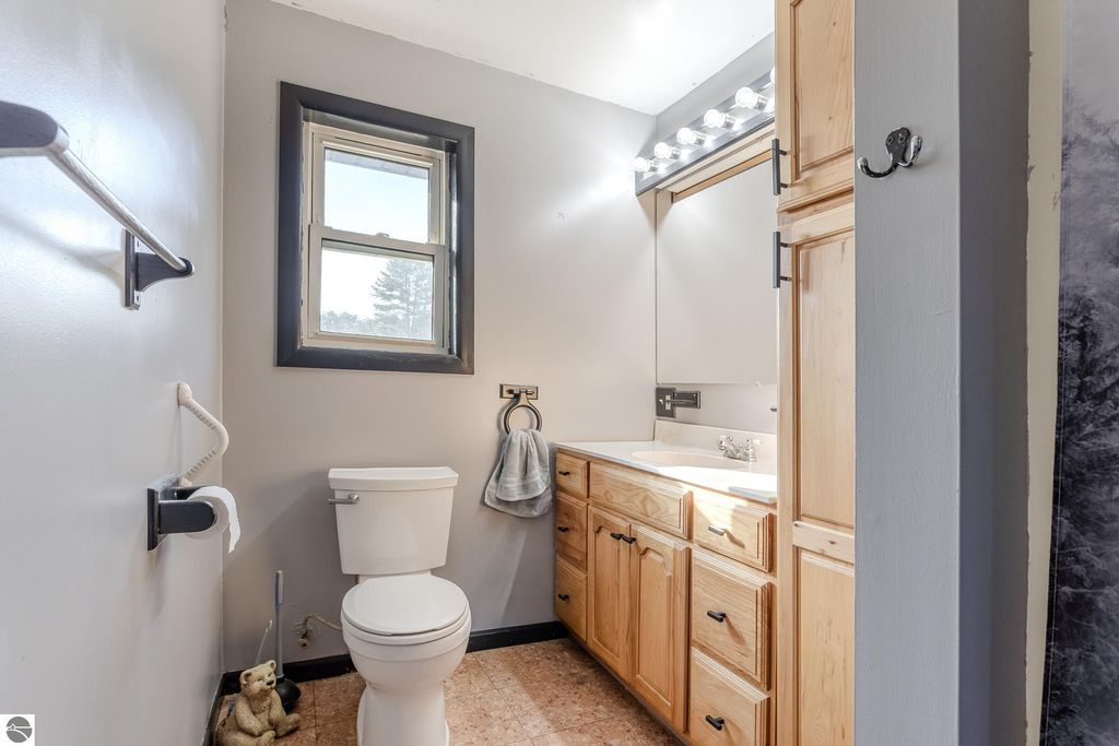 Bathroom interior featuring a toilet, wooden cabinetry with a sink, a mirror, and a window providing natural light, showcasing a clean and functional design.