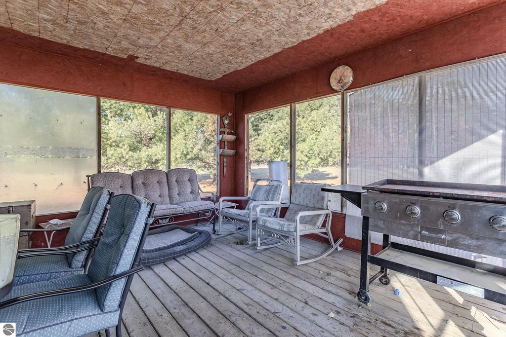 Sunroom with comfortable seating, large windows, and a grill, overlooking a serene outdoor view, part of the property at 2265 Michigan Avenue, Prescott, MI.