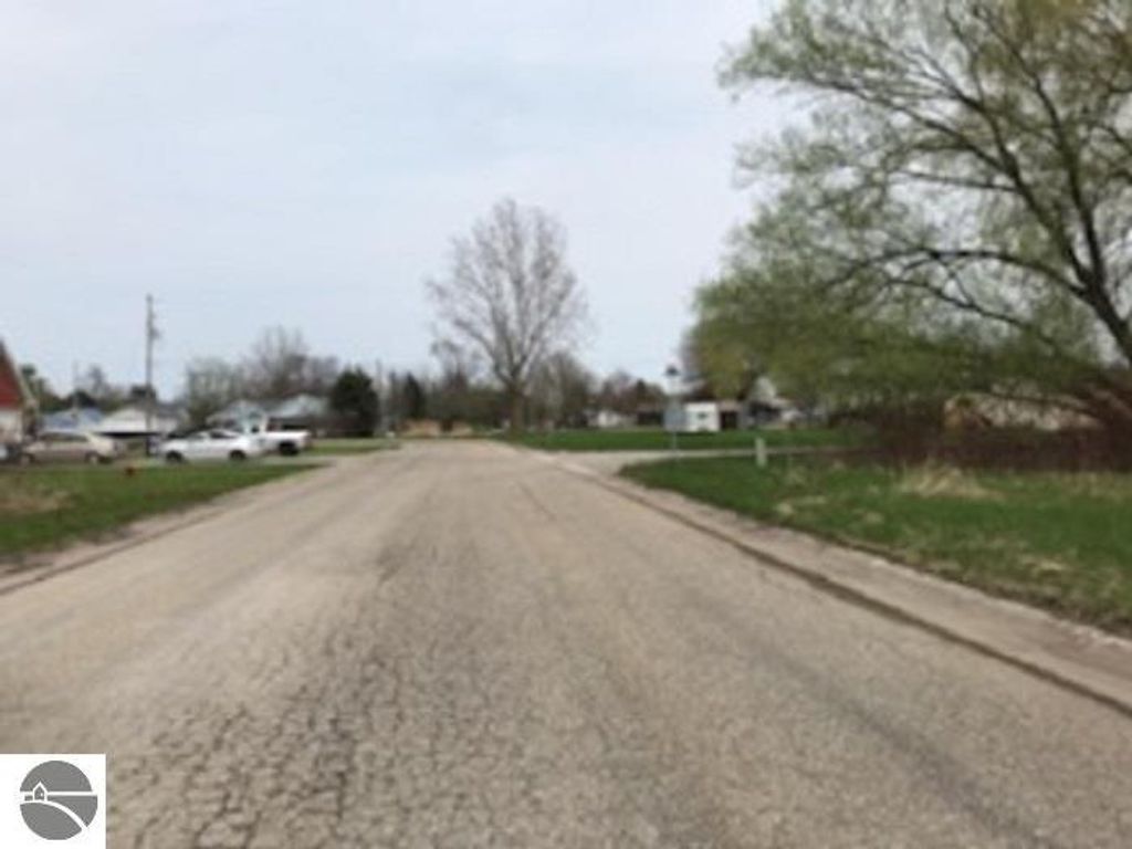 Road view in Au Gres, MI, showcasing potential building site with nearby residential properties and greenery, emphasizing available utilities and location benefits.
