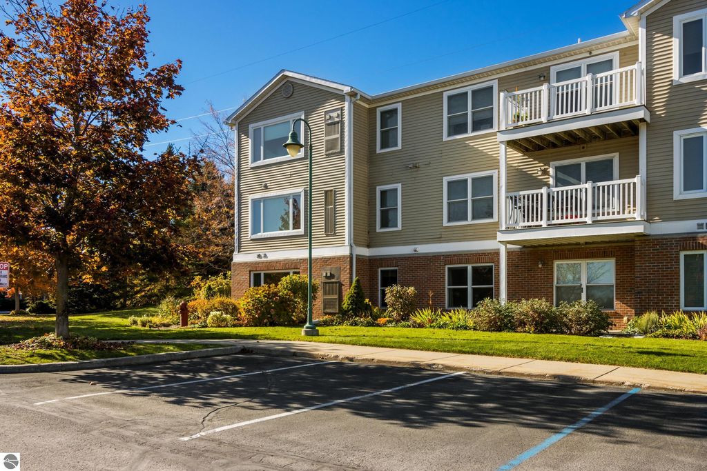Two-story condo building exterior with balconies, landscaped grounds, and autumn foliage, located at 1122 Lake Ridge Drive in Traverse City, MI, showcasing a welcoming atmosphere for residents.