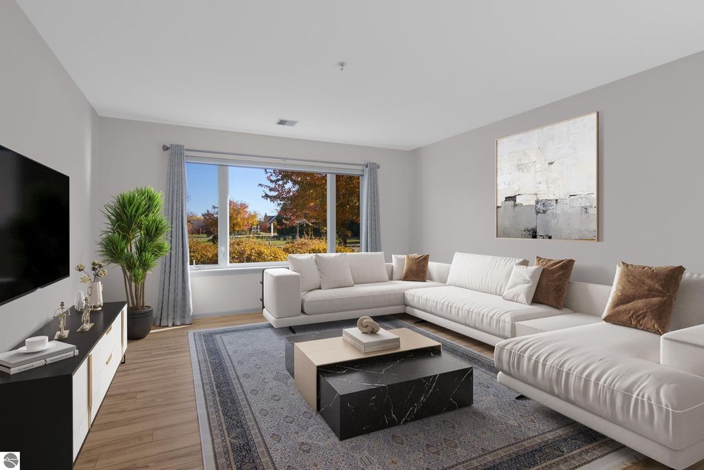 Modern living room in a Traverse City condo, featuring a stylish white sectional sofa, a black coffee table, and large windows with autumn views, showcasing the updated interior design ideal for comfortable lakeside living.