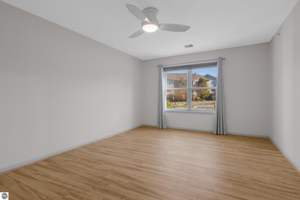 Spacious, updated bedroom in Traverse City condo featuring hardwood floors, large window with natural light, and modern ceiling fan.
