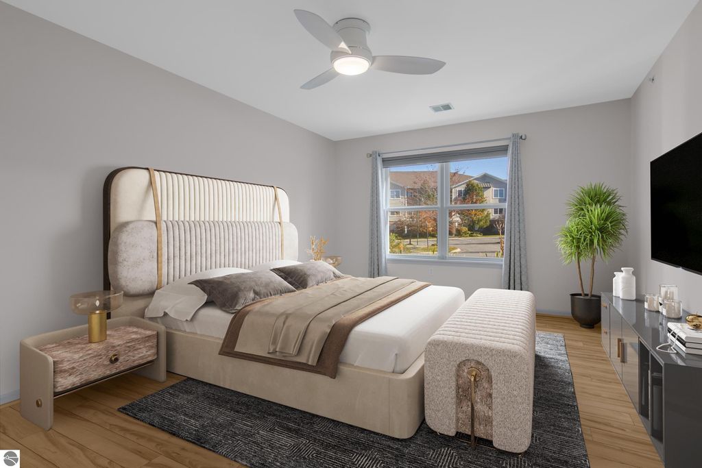 Modern bedroom interior featuring a stylish upholstered bed, decorative throw pillows, bedside table with lamp, and large windows allowing natural light, showcasing a cozy living space in a Traverse City condo.