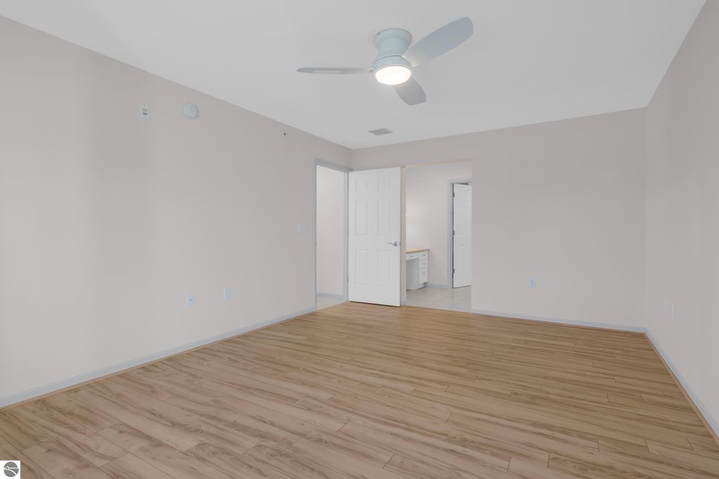 Spacious interior of a 2-bedroom, 2-bathroom condo featuring hardwood flooring, a ceiling fan, and a neutral color palette, with doorways leading to additional rooms, ideal for easy lakeside living in Traverse City, MI.
