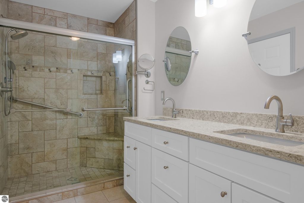 Updated bathroom featuring a spacious walk-in shower with glass enclosure, modern fixtures, dual sinks, and elegant granite countertops in a Traverse City condo.