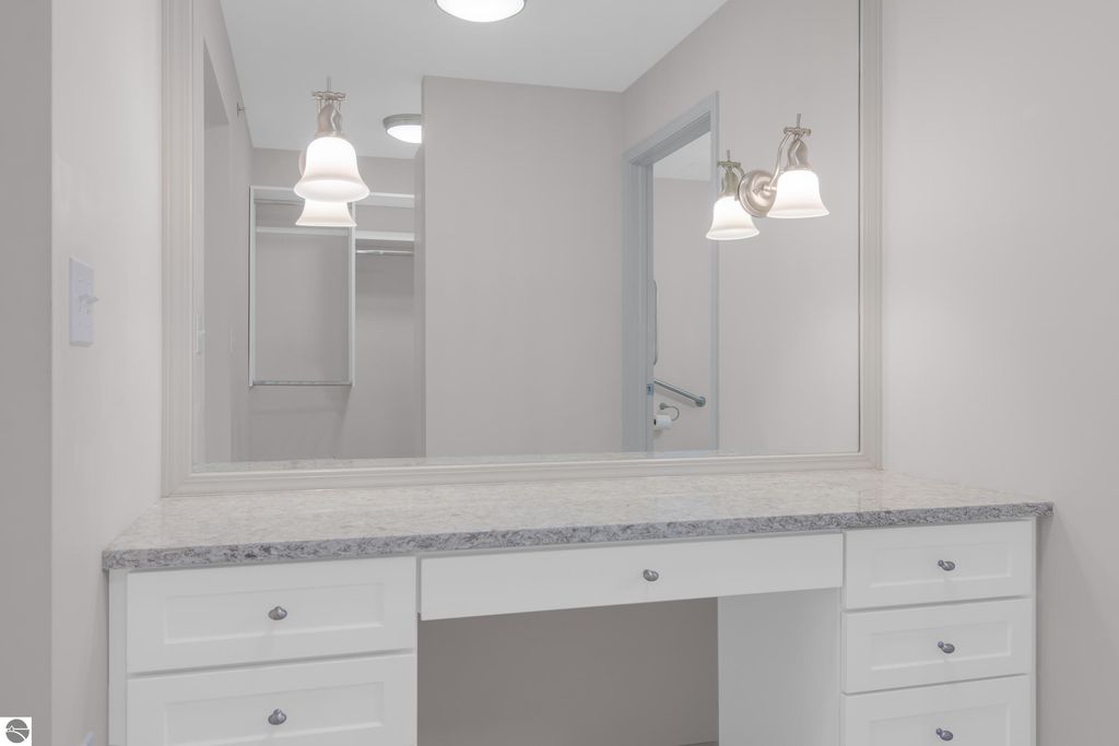 Bathroom vanity with a granite countertop, illuminated by pendant lights, featuring a large mirror and adjacent closet space, showcasing modern design elements in a Traverse City condo.