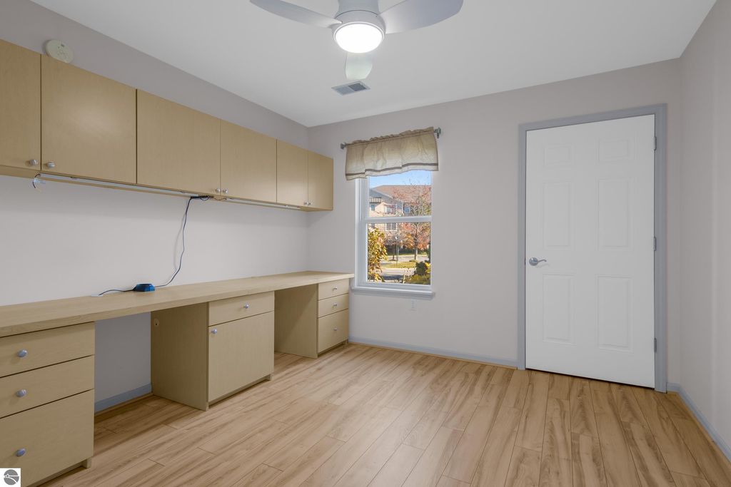 Bright and spacious room with light wood flooring, modern cabinetry, and a window overlooking a landscaped area, suitable for a home office or study in a Traverse City condo.