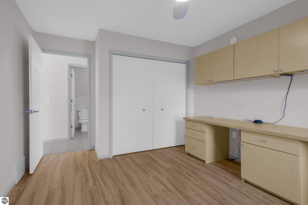 Interior view of a well-lit, updated condo office space featuring a wooden floor, built-in cabinetry, and a doorway leading to a bathroom, reflecting the modern living amenities of the Traverse City listing.