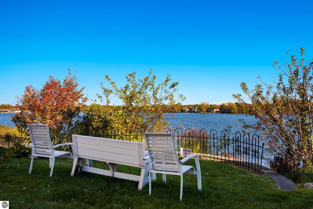 Lakeside view from a condo at 1122 Lake Ridge Drive, featuring white outdoor seating, colorful autumn foliage, and Boardman Lake in the background.