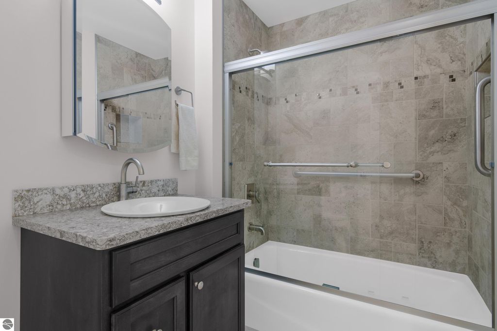 Updated bathroom featuring a modern vanity with granite countertop, round sink, large mirror, and glass shower enclosure with tiled walls, showcasing stylish fixtures and accessibility bars.