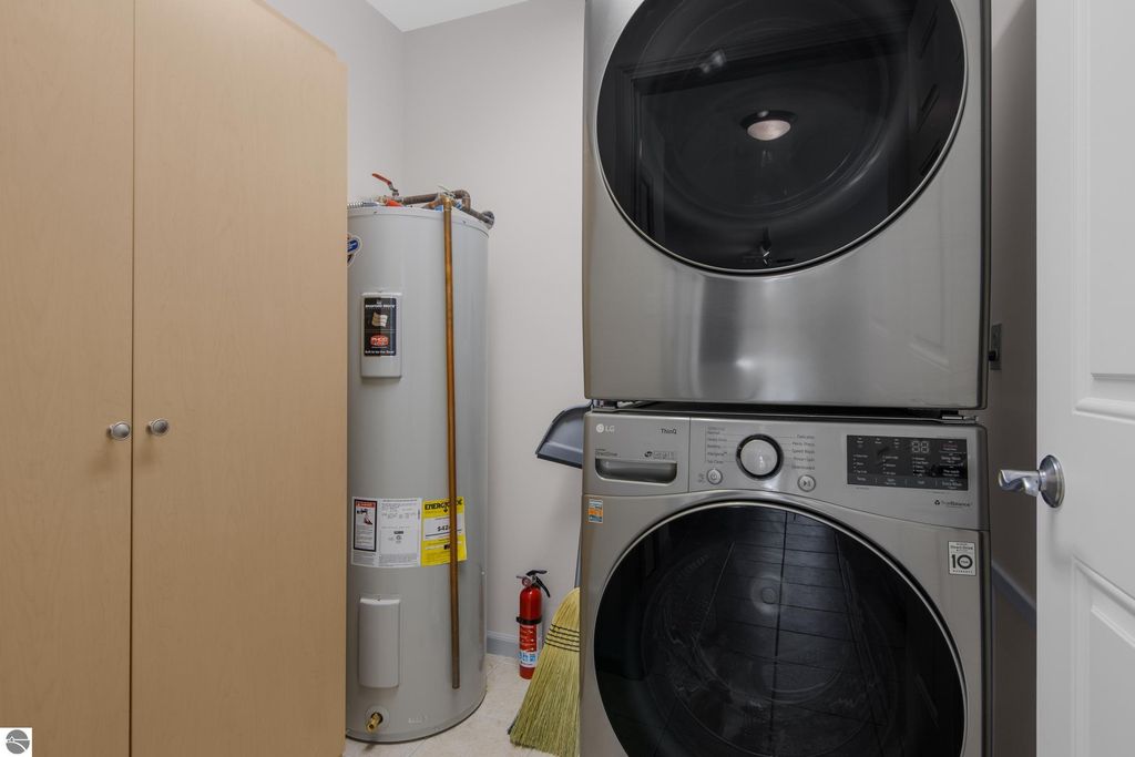 Laundry area featuring stacked LG washer and dryer, adjacent water heater, and storage cabinets in a Traverse City condo.