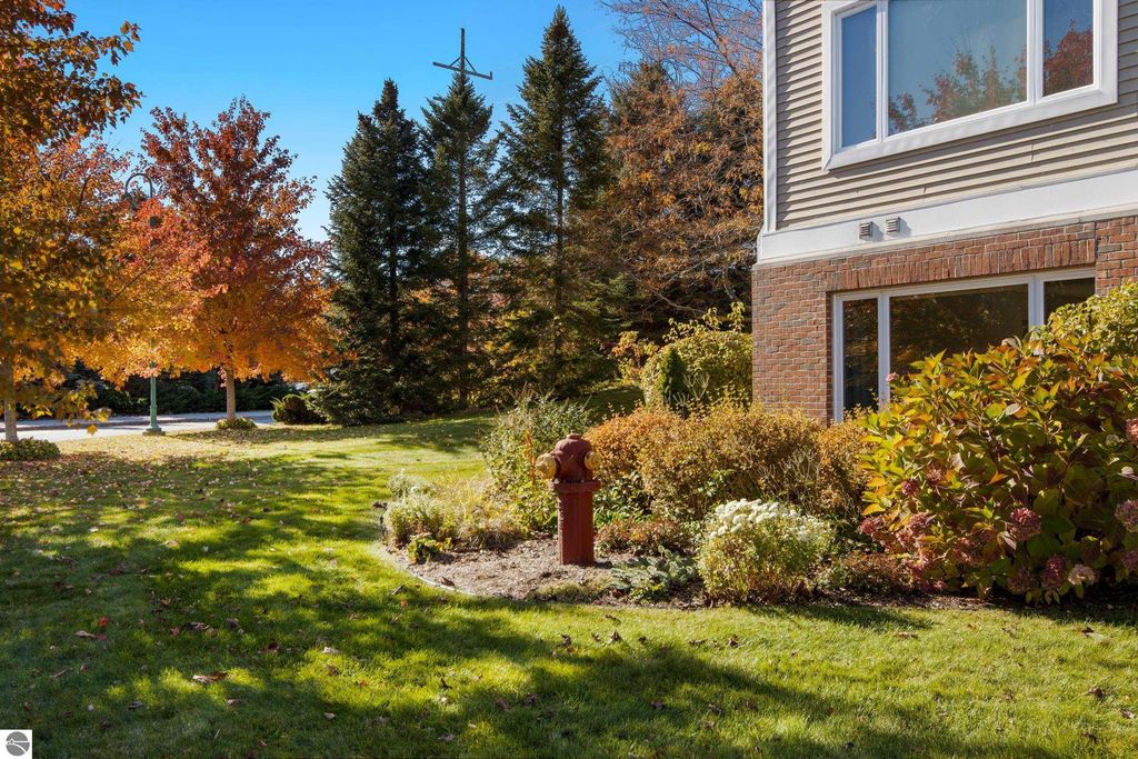 Lakeside condo exterior featuring landscaped garden, colorful autumn foliage, and a visible fire hydrant near 1122 Lake Ridge Drive #103, Traverse City, MI.
