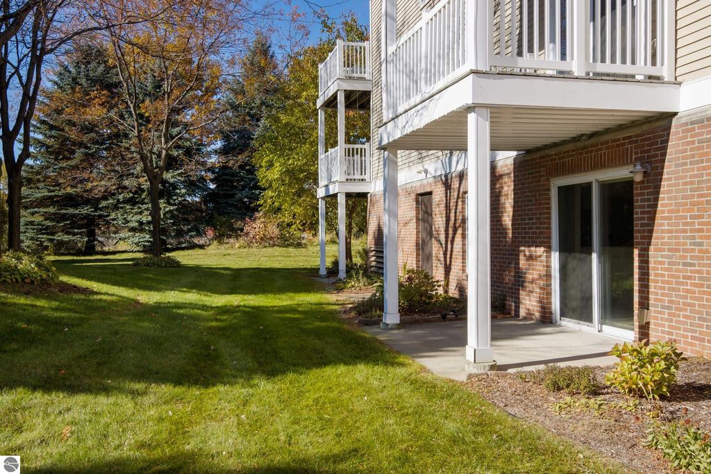 Ground-level view of a condo patio area at 1122 Lake Ridge Drive, featuring landscaped greenery, a brick exterior, and shaded trees, highlighting the outdoor space for the 2BR/2BA property near Boardman Lake.