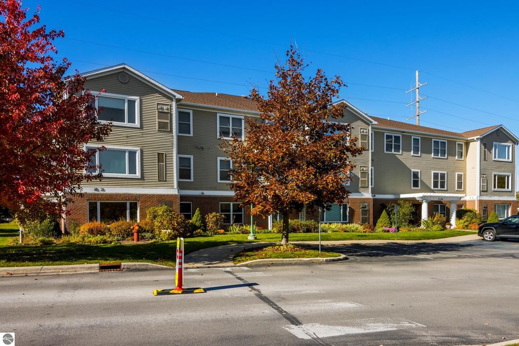 Condo building exterior at 1122 Lake Ridge Drive, Traverse City, MI, featuring landscaped grounds and autumn foliage, highlighting the property for sale.