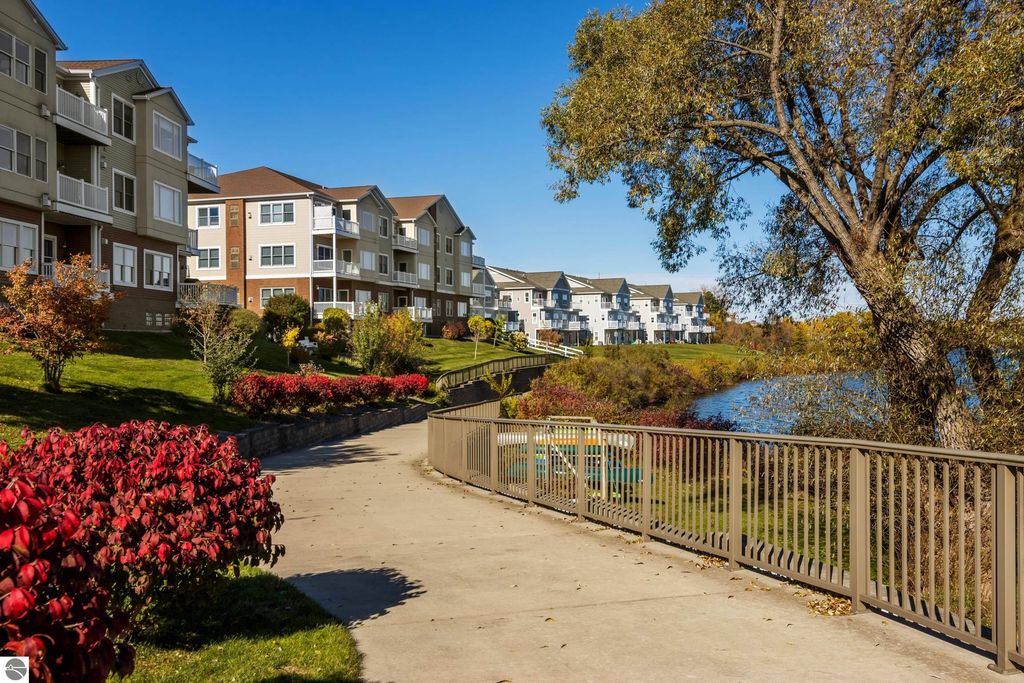 Lakeside view of updated condominium complex in Traverse City, MI, featuring landscaped grounds, walking path, and Boardman Lake in the background.