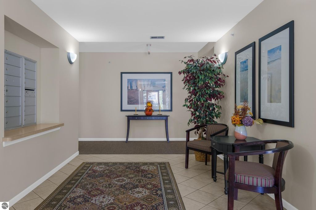 Condo lobby with mailboxes, decorative plants, framed artwork, and seating area, showcasing welcoming first-floor living at 1122 Lake Ridge Drive, Traverse City.