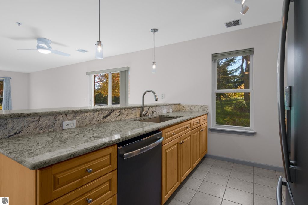 Updated kitchen with granite countertops, wooden cabinetry, stainless steel appliances, and windows showcasing outdoor views in a Traverse City condo.