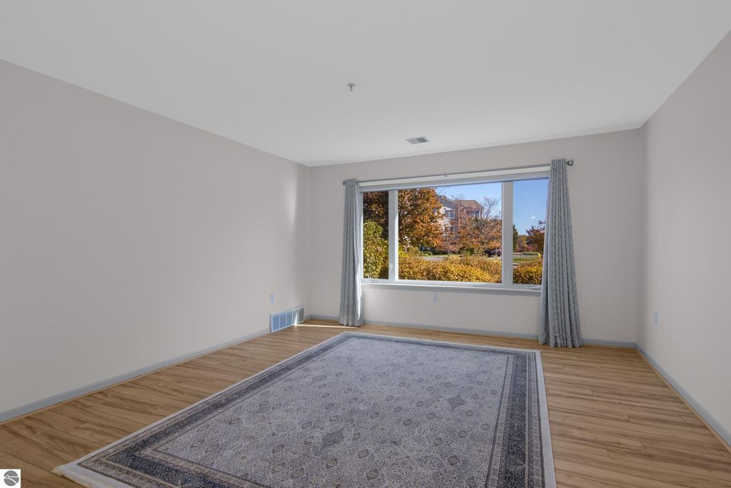 Spacious living area of a condo in Traverse City, featuring large windows with natural light, hardwood floors, and a decorative area rug, ideal for lakeside living.