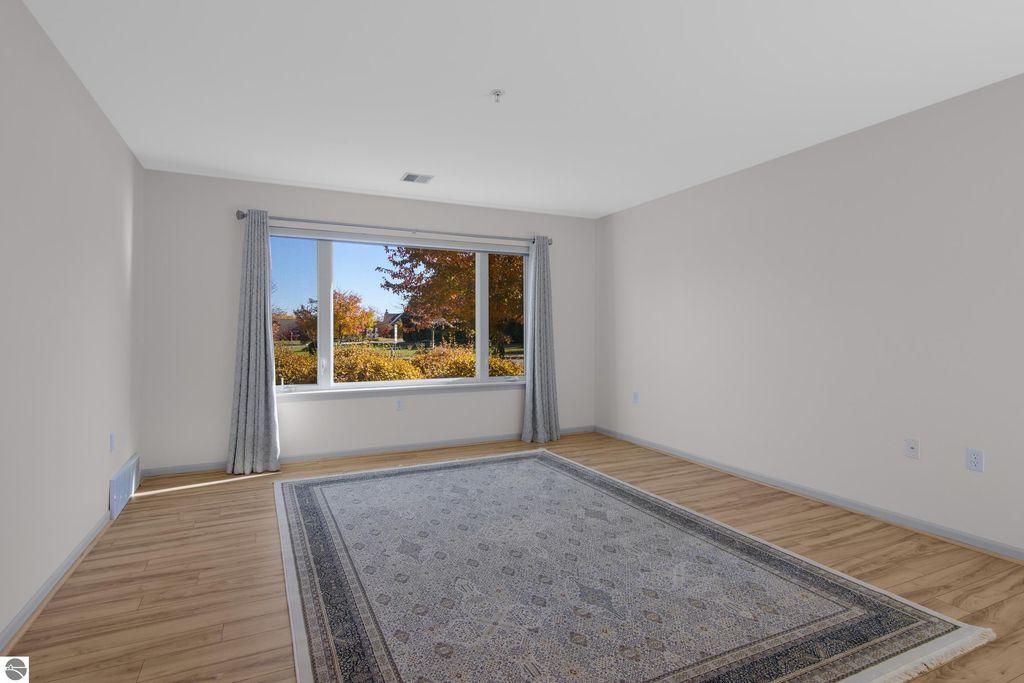 Bright, spacious living area in a condo at 1122 Lake Ridge Drive, featuring large windows with autumn views, hardwood flooring, and a decorative area rug.