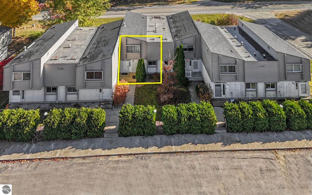 Aerial view of a remodeled townhouse at 10759 S Timberlee Drive #4 in Traverse City, Michigan, showcasing a two-story structure with landscaped greenery and a clear pathway, emphasizing the property’s inviting exterior and proximity to surrounding amenities.