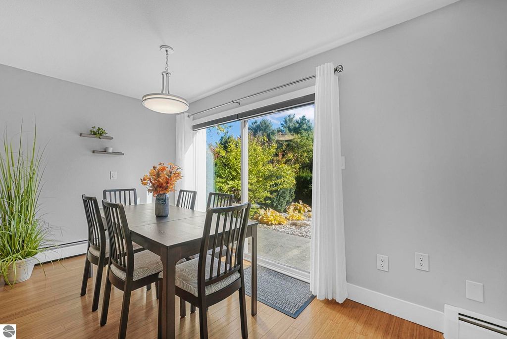 Dining area of a remodeled townhouse in Traverse City, featuring a wooden table with chairs, a vase of flowers, and a view of the landscaped backyard through sliding glass doors.