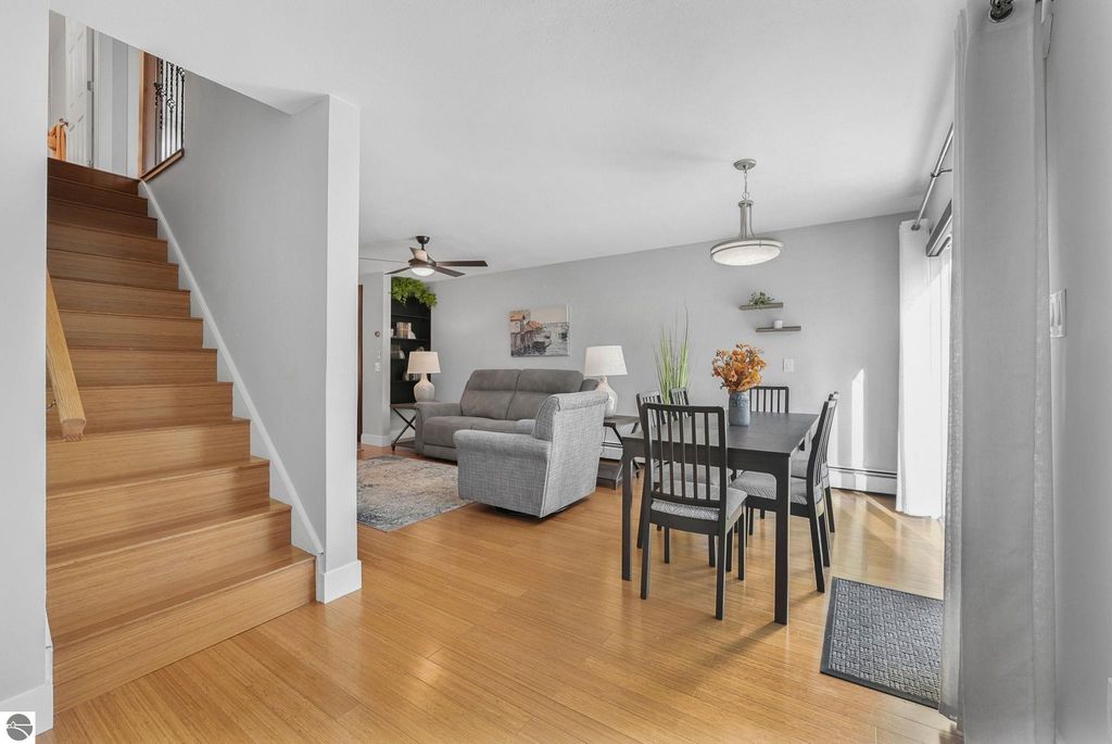 Bright and open living area in remodeled townhouse, featuring wooden staircase, dining table, and comfortable seating, showcasing modern decor and natural light, located in Traverse City, MI.