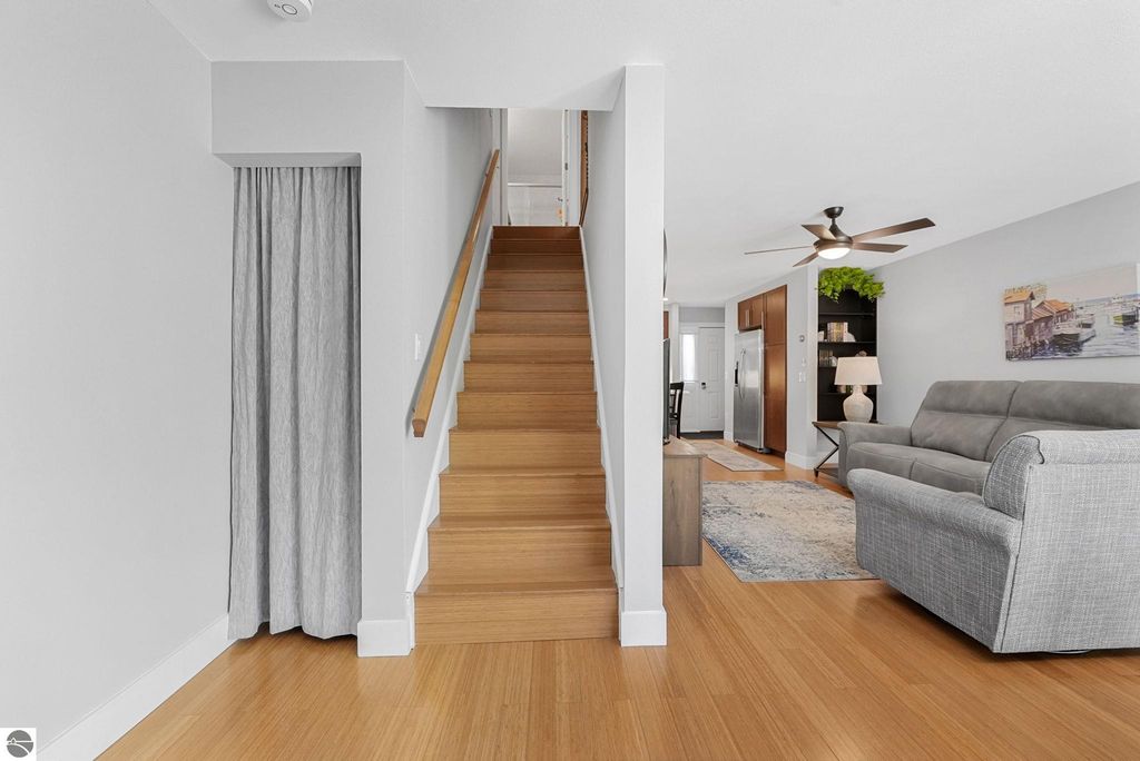 Bright and open interior of a remodeled townhouse in Traverse City, featuring a wooden staircase, gray sofa, and modern kitchen area visible in the background.