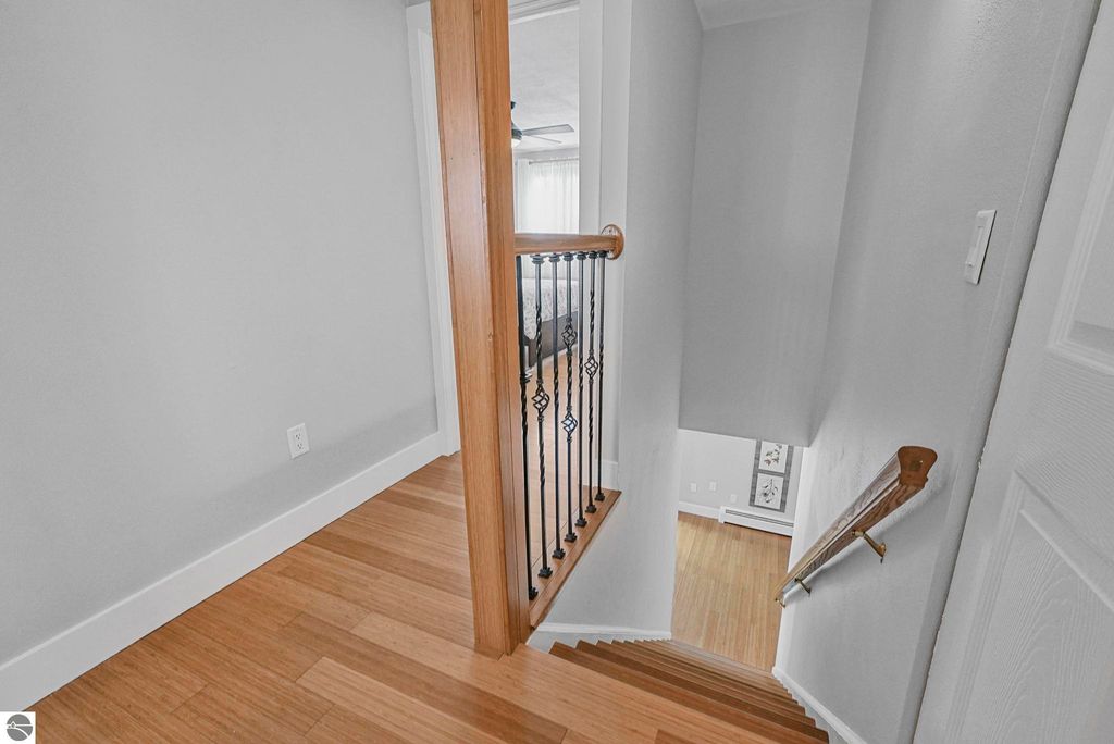 Staircase view in remodeled townhouse, featuring wood flooring, iron railing, and natural light, leading to upper level bedrooms in Traverse City, MI.