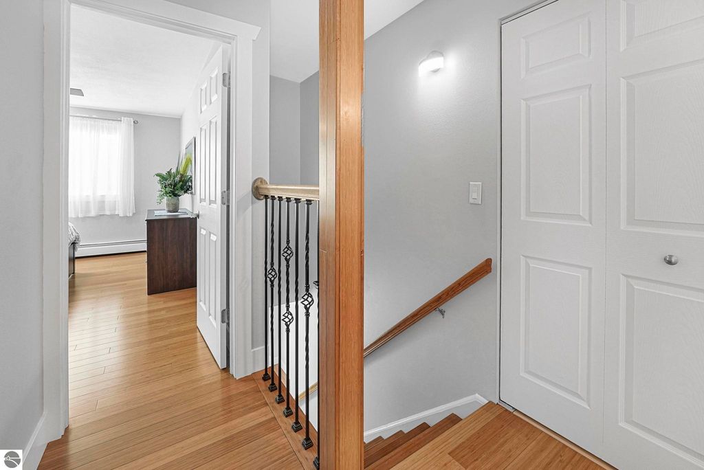 Bright and inviting interior view of a remodeled townhouse in Traverse City, featuring bamboo flooring, a staircase with decorative railing, and an open doorway leading to a bedroom with natural light.