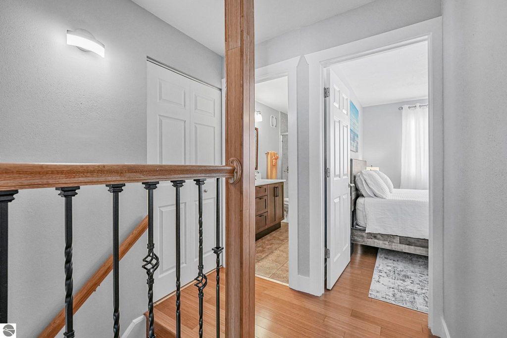 Interior view of remodeled townhouse in Traverse City, showcasing hallway with wood flooring, light fixtures, and access to bathroom and bedroom.