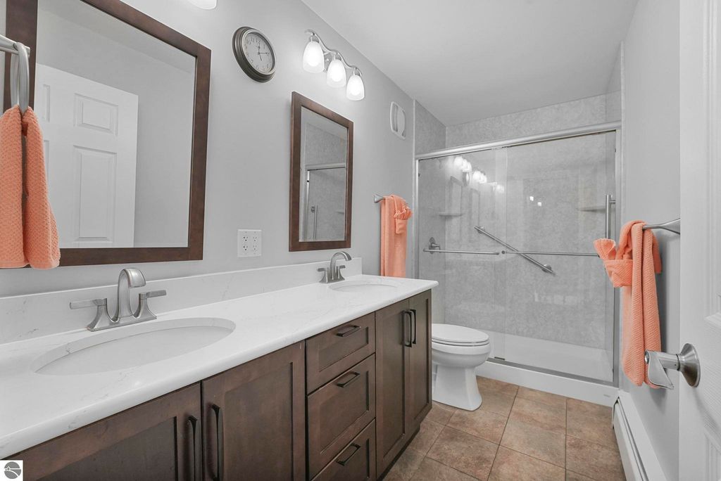 Modern bathroom featuring double sinks, dark wood cabinetry, and glass shower enclosure, complemented by orange towels and neutral color scheme.
