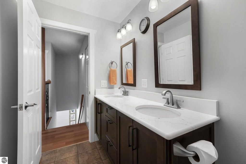 Modern bathroom with dual sinks, dark wood cabinetry, and large mirrors, featuring a neutral color palette and natural light from the adjacent hallway.