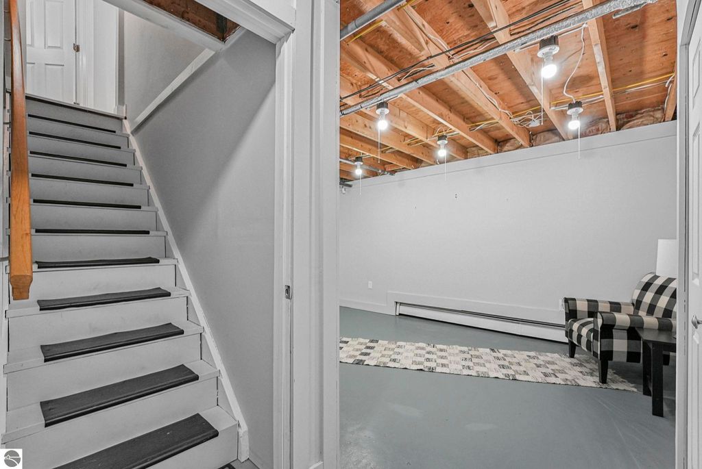 Staircase leading to upper level of remodeled townhouse with spacious lower level featuring gray flooring and modern lighting.