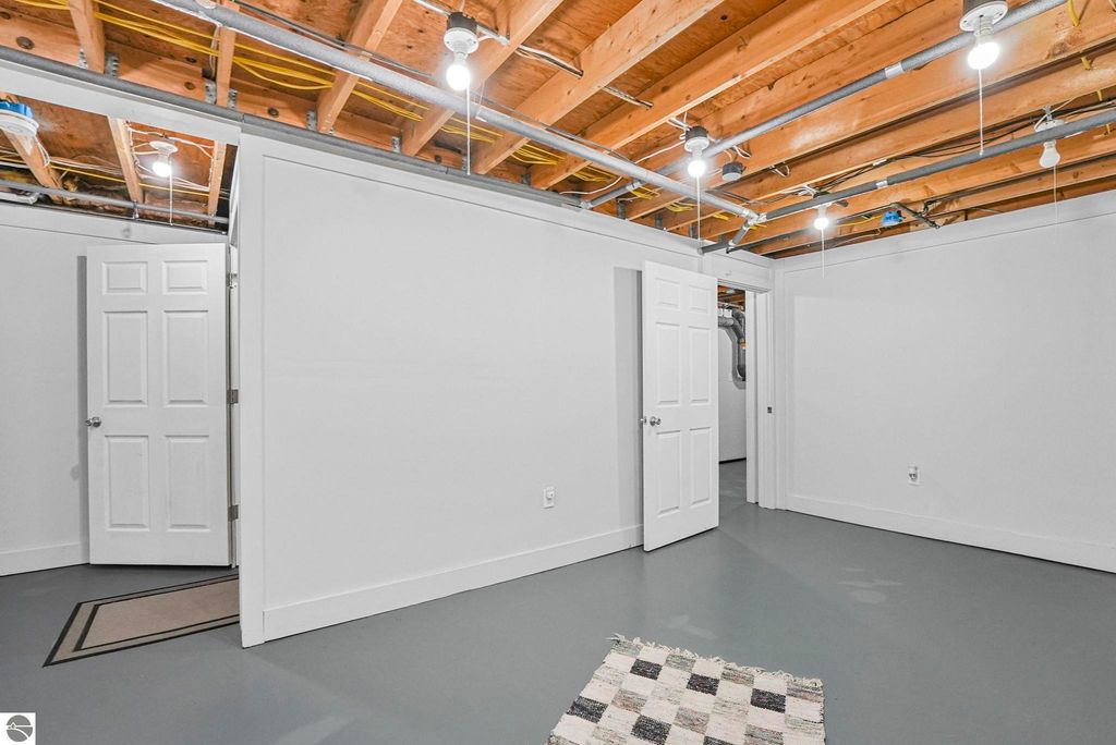 Bright and spacious lower level of townhouse in Traverse City, featuring freshly painted walls, modern lighting, and multiple doors leading to storage areas.