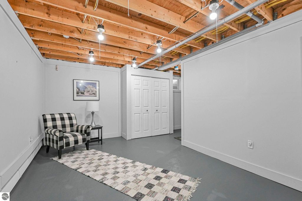 Bright and open lower level of a remodeled townhouse in Traverse City, featuring a black and white checkered chair, a lamp, framed artwork, and a decorative rug on polished concrete flooring.