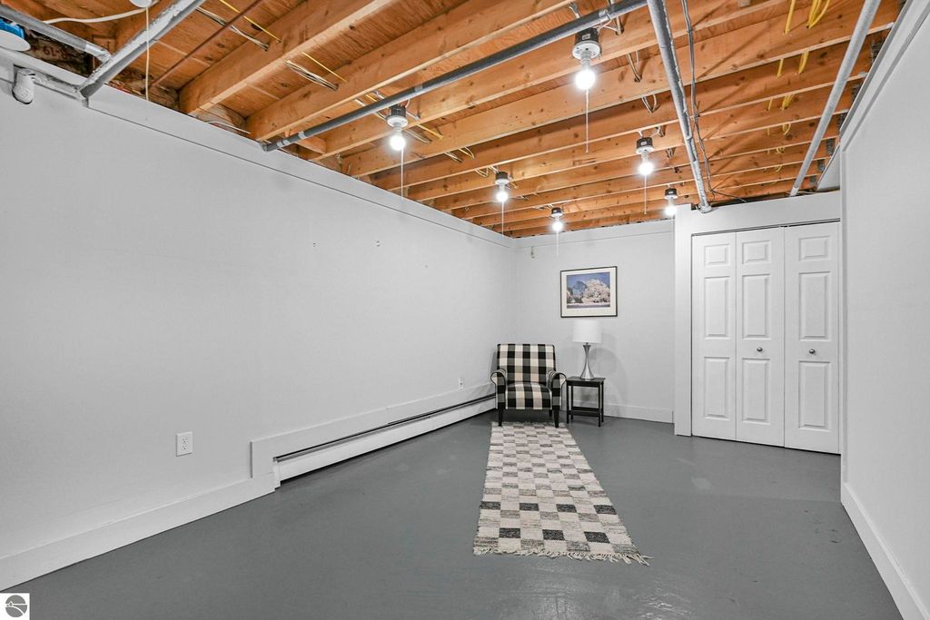 Bright, spacious lower level of townhouse in Traverse City, featuring a checkered rug, a striped chair, and closet doors, showcasing potential for additional living or storage space.