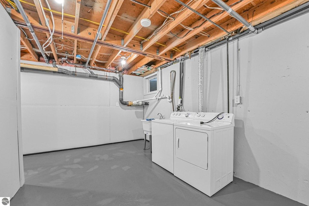 Basement laundry area featuring a washer and dryer, exposed wooden beams, and plumbing details in a remodeled Traverse City townhouse.
