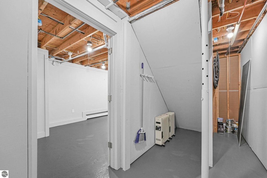 Interior view of a basement space in a Traverse City townhouse, featuring gray flooring, exposed wooden beams, a heating unit, and storage options, highlighting the additional space available for storage or utility use.