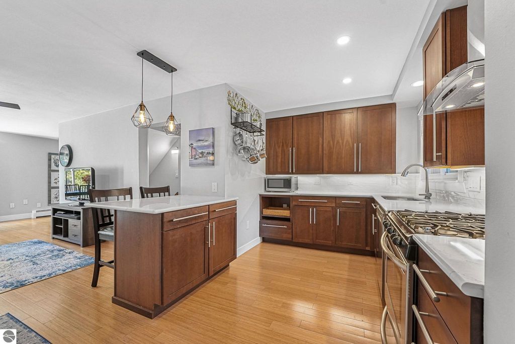 Modern kitchen interior with wood cabinetry, quartz countertops, stainless steel appliances, and a dining area featuring a table and chairs, showcasing a bright and open design in a Traverse City townhouse.