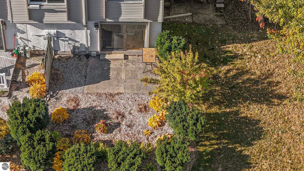 Aerial view of the rear patio and landscaped yard of a townhouse in Traverse City, featuring colorful autumn foliage, a concrete patio area with a small table, and well-maintained shrubs.