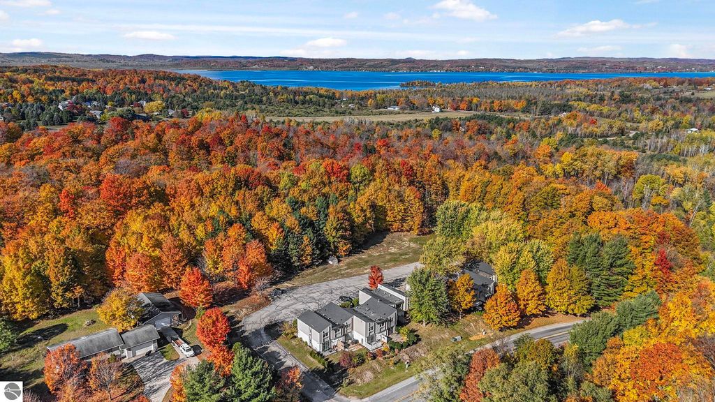Aerial view of colorful autumn foliage surrounding a townhouse in Traverse City, Michigan, near a lake, showcasing the vibrant fall landscape and nearby residential area.