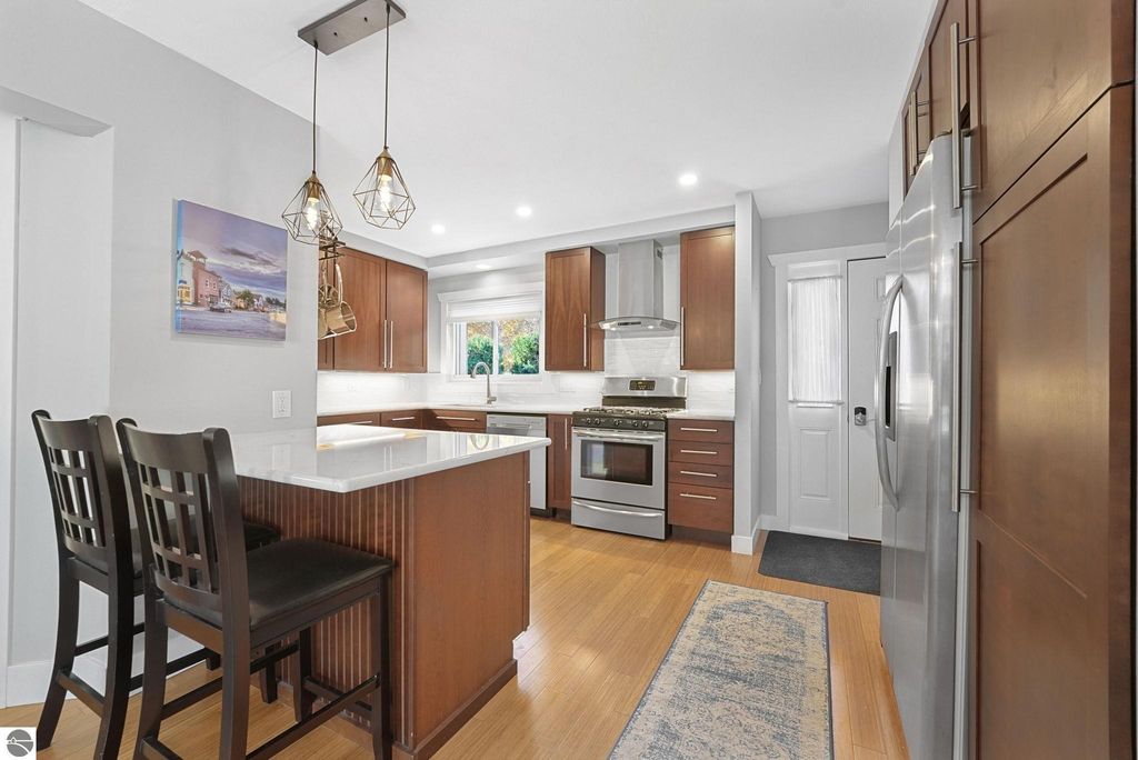 Modern kitchen with quartz countertops, stainless steel appliances, and open layout, featuring wood flooring, pendant lighting, and seating area, showcasing a bright and inviting space in Traverse City townhouse.
