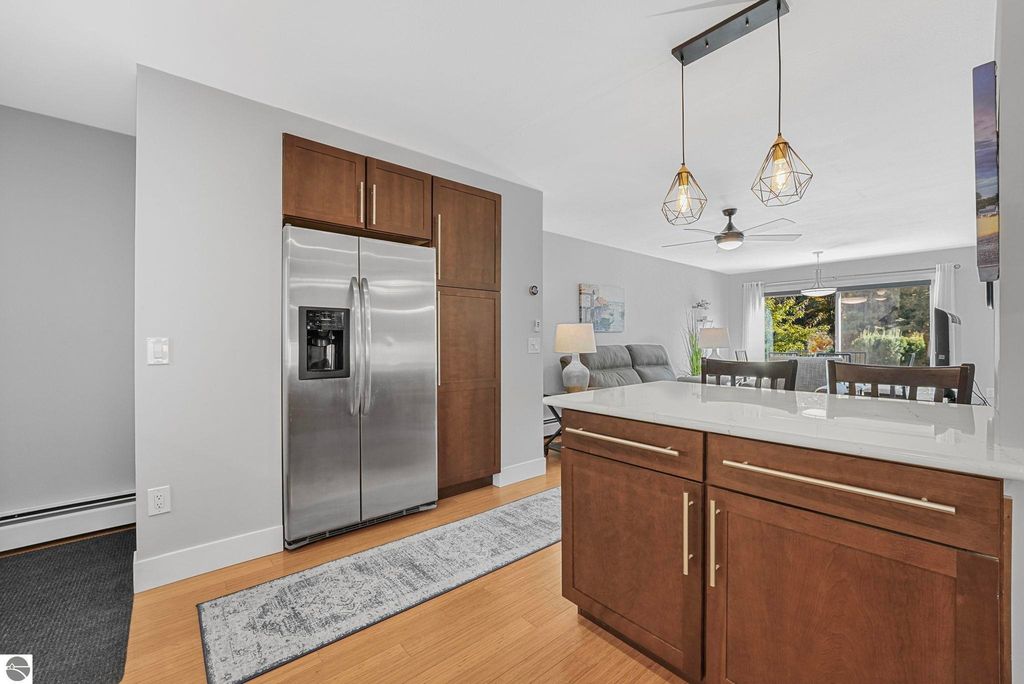 Modern kitchen featuring stainless steel refrigerator, quartz countertops, and wooden cabinetry, with open living space and natural light from large windows in Traverse City townhouse.
