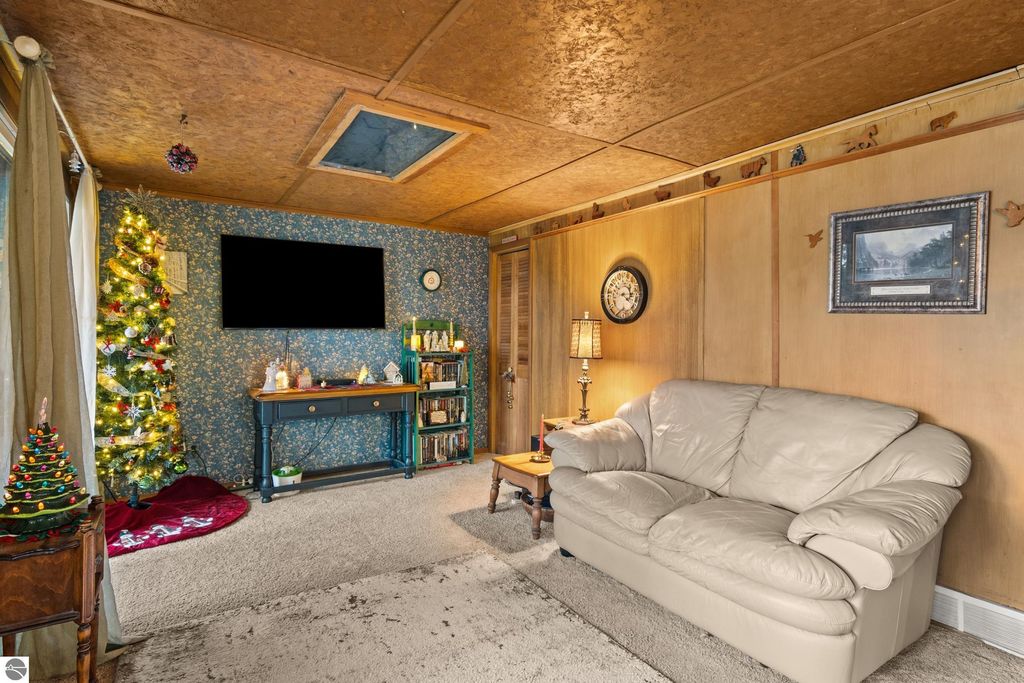 Cozy living room featuring a Christmas tree, soft beige couch, decorative wall art, and a television mounted on a blue wallpapered wall, ideal for relaxed Up North living at 4411 Lakeview Trail, Traverse City, MI.