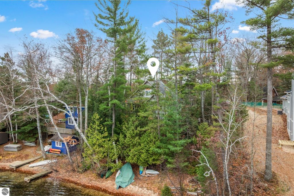 Waterfront view of a wooded property at 4411 Lakeview Trail, featuring a sandy shoreline along Spider Lake, surrounded by trees and nearby cabins, ideal for Up North living.