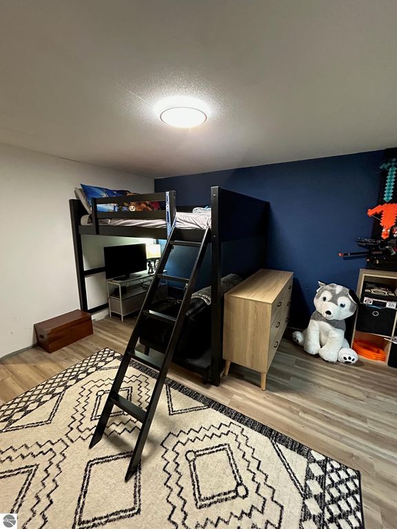 Cozy bedroom featuring a lofted bed with a ladder, modern dresser, and a plush toy, set against a dark blue wall and a patterned area rug.