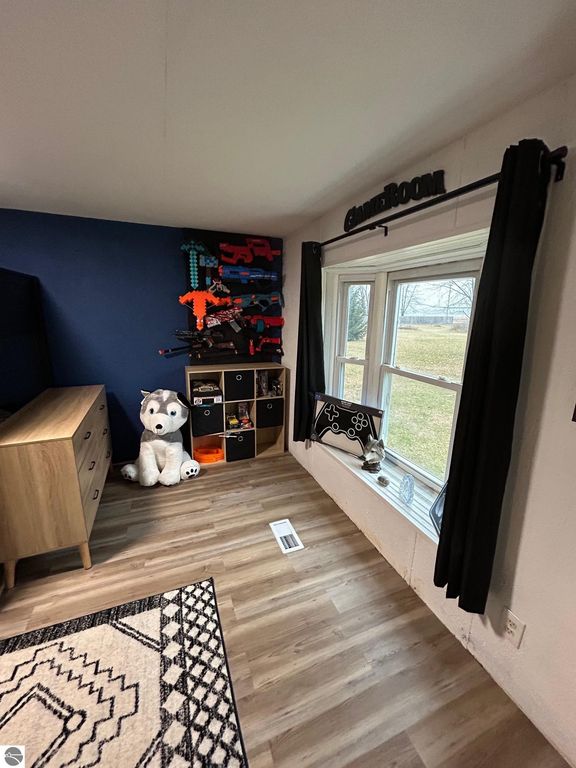 Cozy game room featuring a blue accent wall, plush husky toy, storage unit with colorful toy guns, and a window with views of the outdoors.