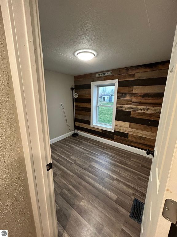 Interior view of a room featuring a wood-paneled accent wall, a window with a view of the outdoors, a floor lamp, and new laminate flooring, showcasing updates in the property for sale at 3780 E North County Line Road, St Louis, MI.