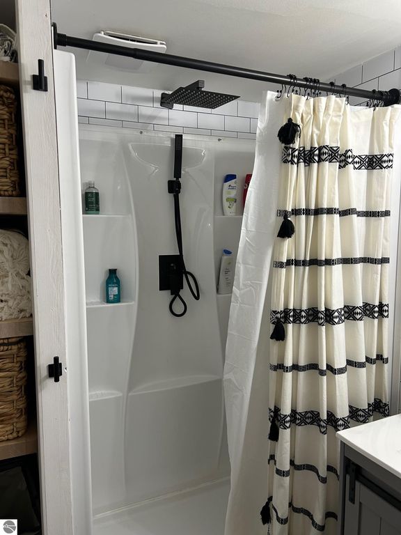 Updated bathroom shower with modern fixtures, white shower curtain, and storage shelves, showcasing a clean and stylish design relevant to the property at 3780 E North County Line Road, St Louis, MI.