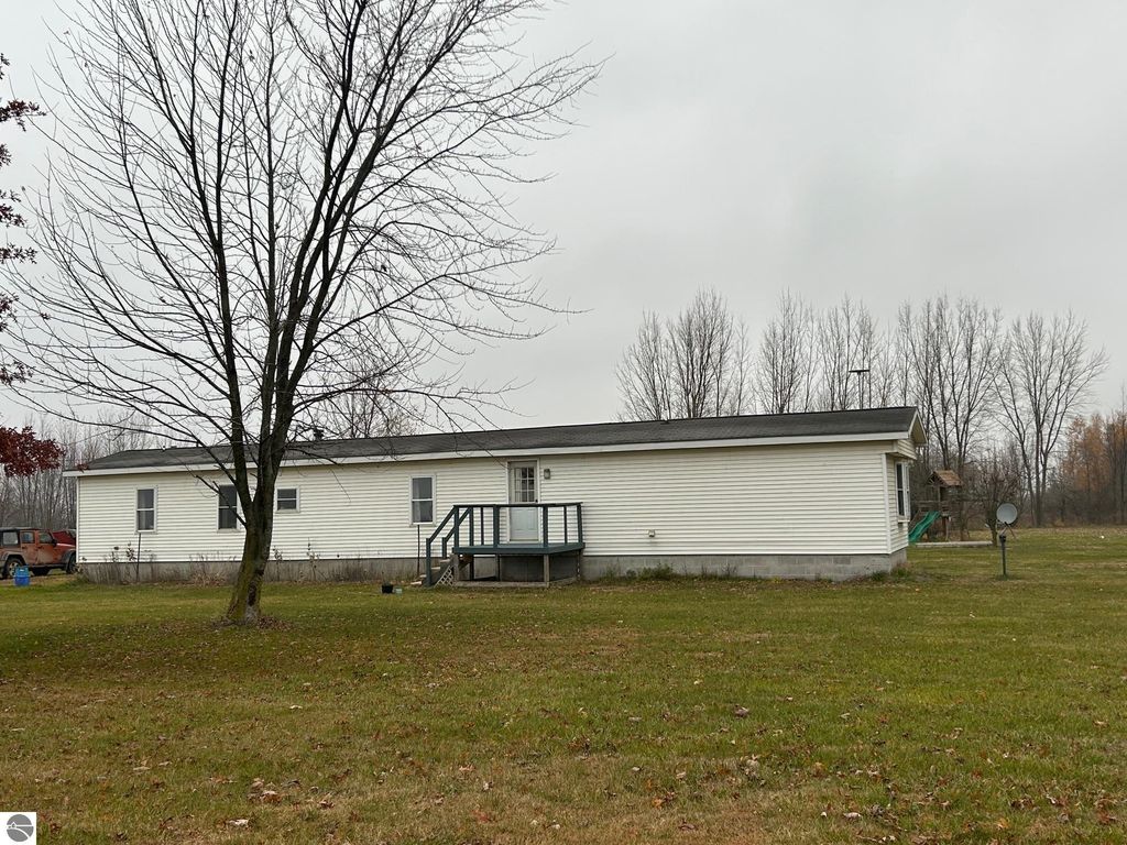 Single-story residential property with a front porch, surrounded by grassy yard and trees, located on 1.87 acres in St. Louis, MI, showcasing country living and updated features.